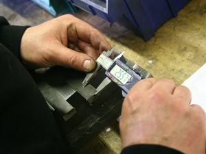 Hands measuring a metal part with a digital caliper