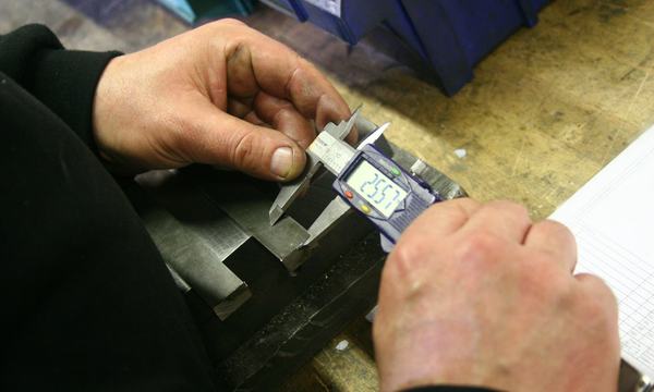 Hands measuring a metal part with a digital caliper