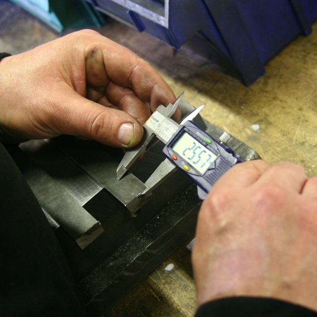Hands measuring a metal part with a digital caliper